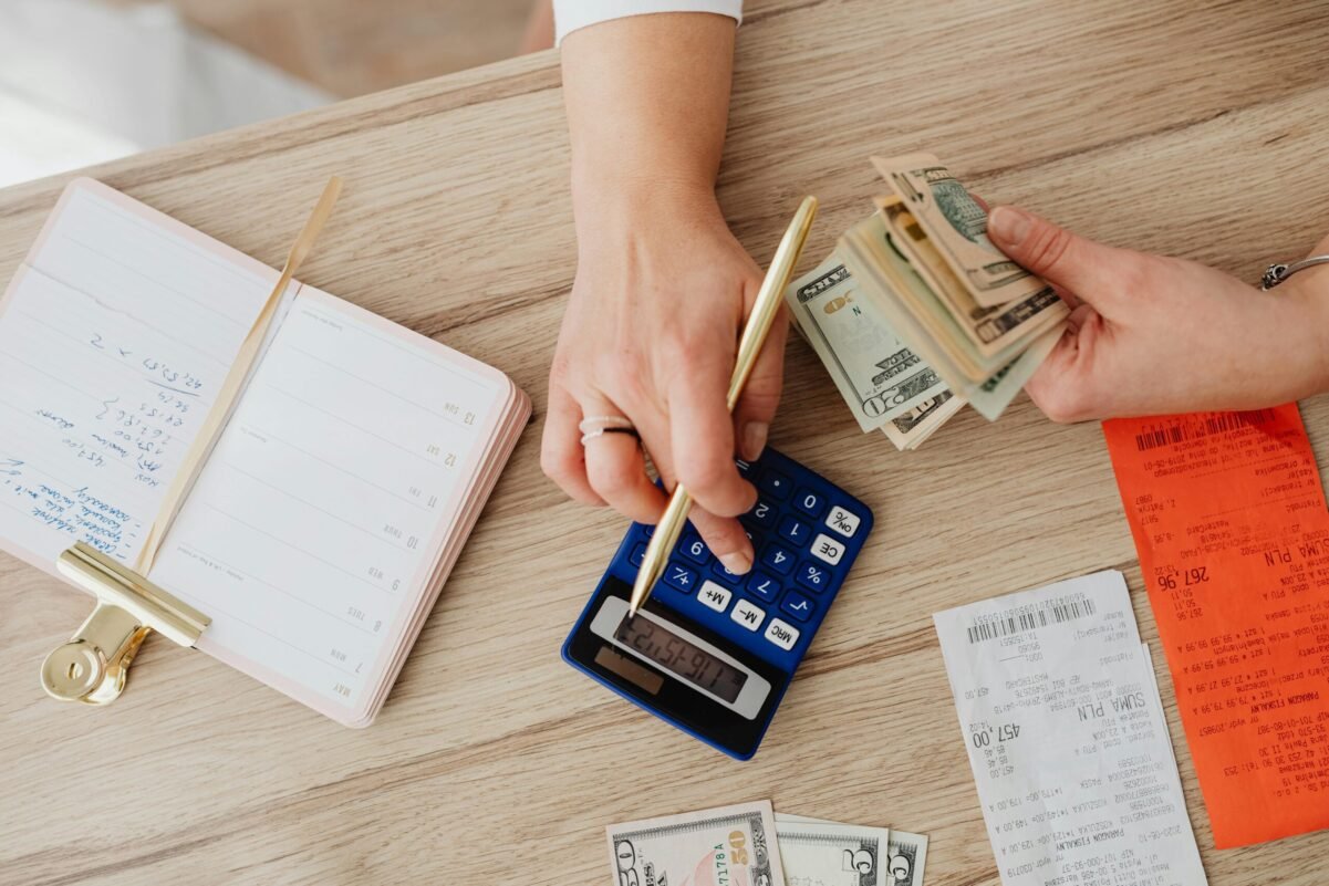 Home Hands managing finances with calculator, cash, and receipts on a wooden table. Ideal for budgeting concepts.